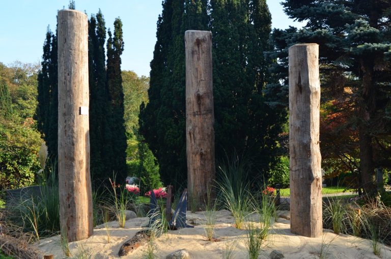 Drei hohe Dalben stehen auf einer kleinen Düne zwischen grünen Pflanzen.