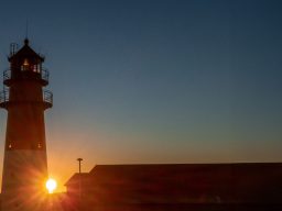 Leuchtturm vor atemberaubendem Sonnenuntergang am Horizont.