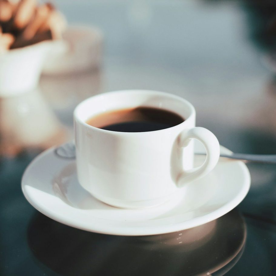 Tasse mit schwarzem Kaffee auf einem Tisch, daneben ein Teller mit Keksen.