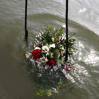 Ein Kranz aus roten und weißen Blumen sinkt in einen Gewässer.