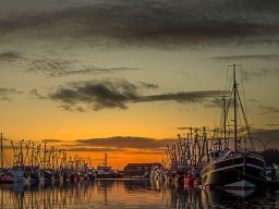 Hafen mit Booten unter einem orangefarbenen Sonnenuntergang und bewölktem Himmel.